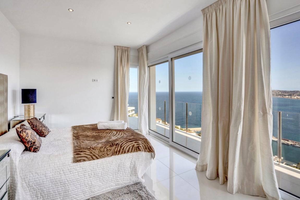 Suite bedroom featuring white polished flooring, floor-to-ceiling glass doors, and direct access to a private balcony overlooking the Mediterranean Sea and Jávea port.