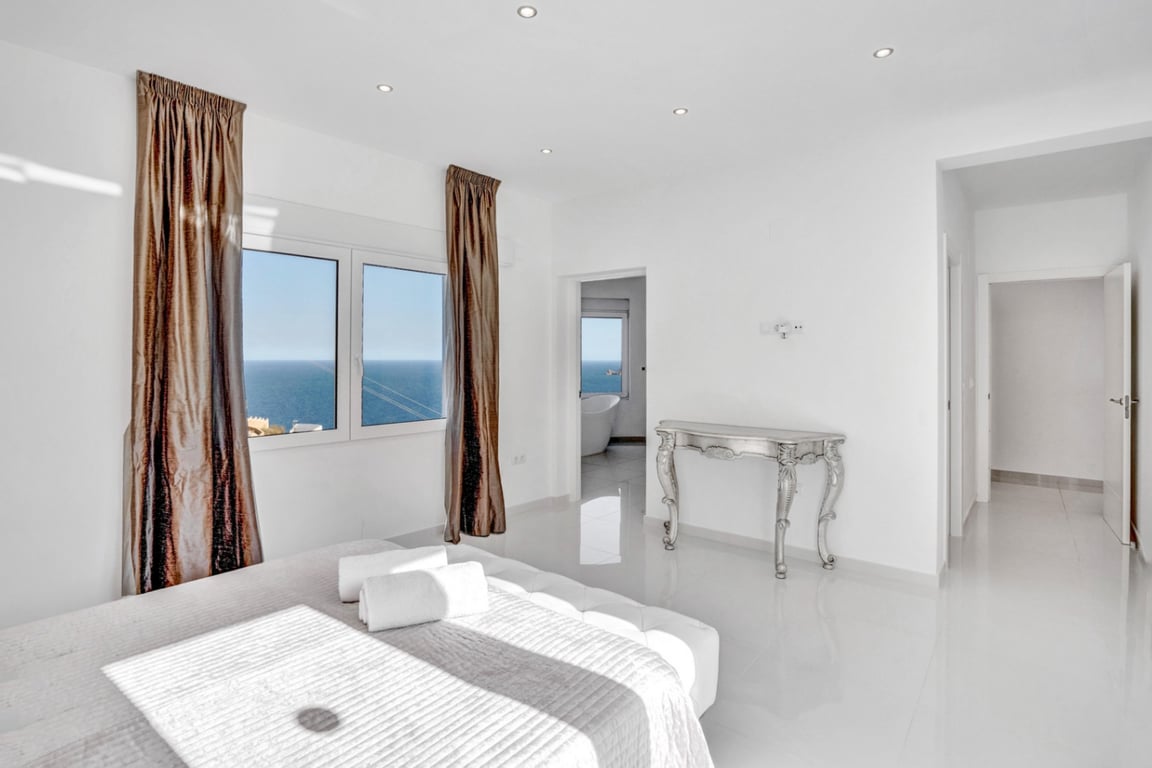 Suite bedroom featuring white porcelain floors, sea views through large windows, and an en-suite bathroom with a freestanding bathtub and coastal vistas.