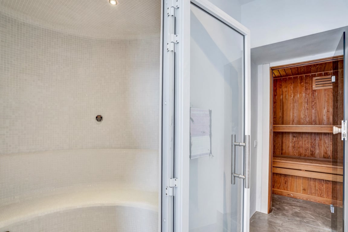 Wellness area featuring a white mosaic-tiled steam room with curved seating adjacent to a classic wood-paneled Finnish sauna.