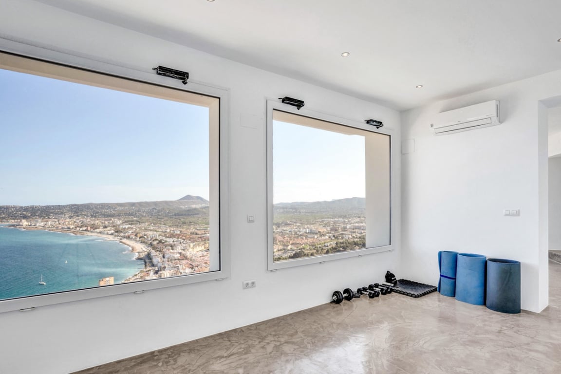 Yoga and fitness area featuring polished microcement floors and large windows with panoramic views of the Mediterranean Sea and Jávea coastline.