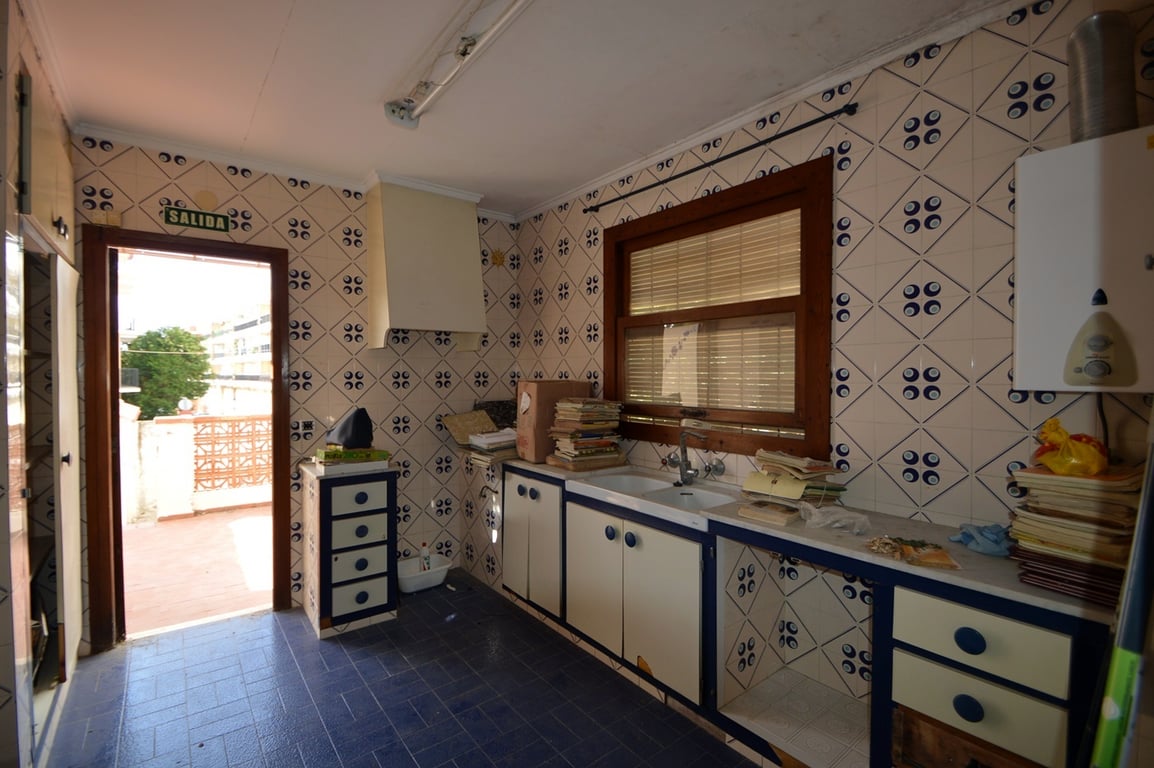Kitchen featuring patterned wall tiles, blue flooring, and direct terrace access. It includes a double sink, wooden-framed window, and cabinetry with blue accents.