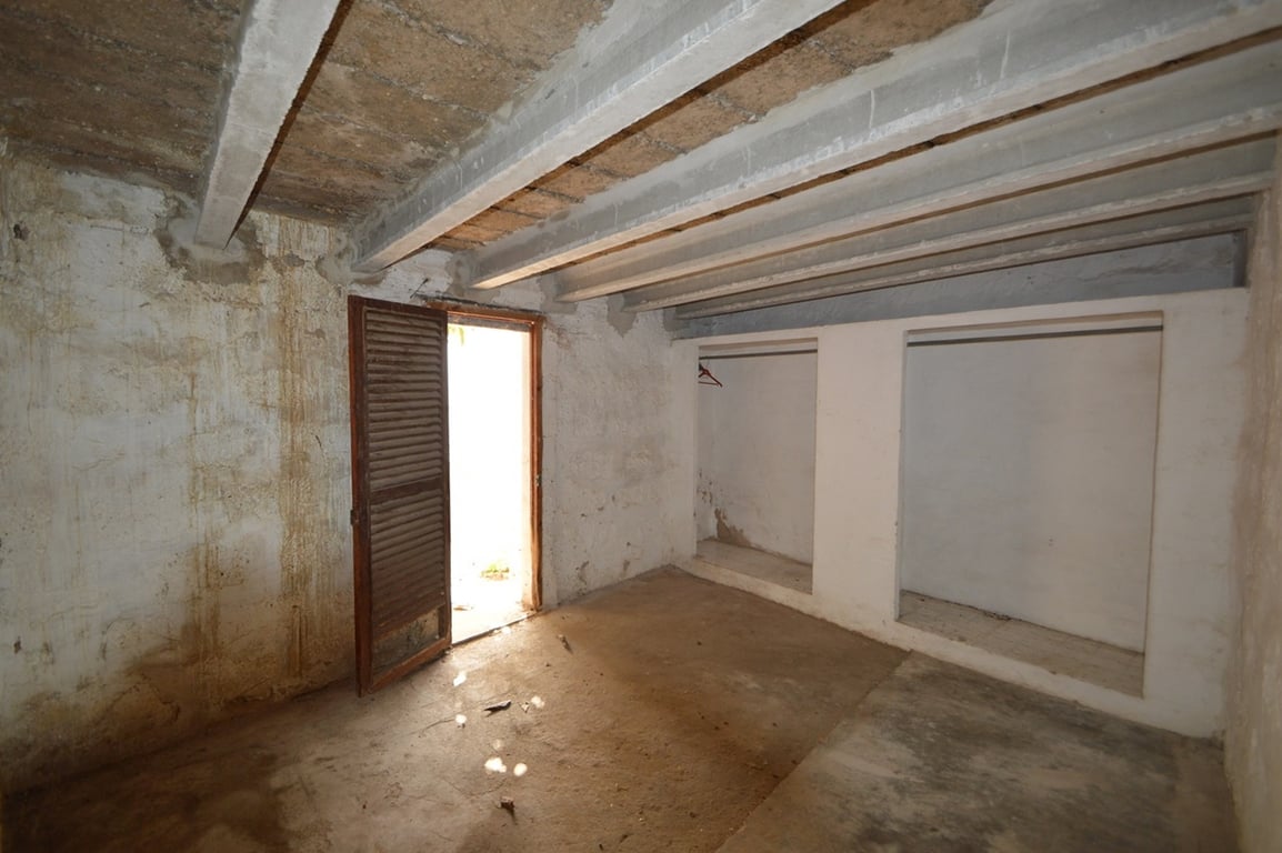 Large storage area featuring exposed ceiling beams, built-in wall niches, and a wooden louvered door providing natural light and outdoor access.