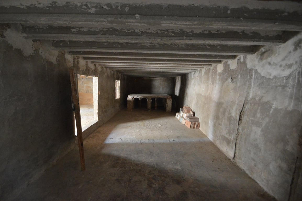Large unfinished open space featuring exposed concrete beams, stone walls, and a built-in stone bench, offering potential for a studio or storage area.