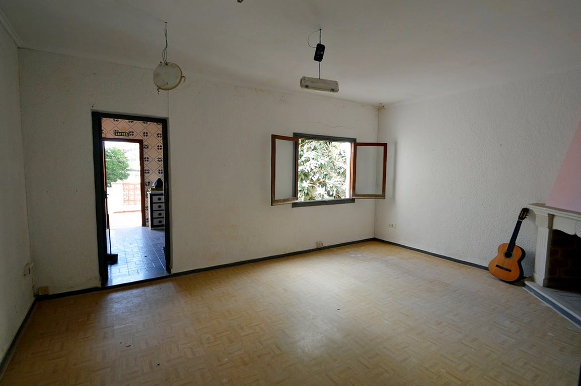 Living room featuring a classic fireplace, patterned flooring, and a window with wooden shutters. The space connects directly to the outdoor patio area.