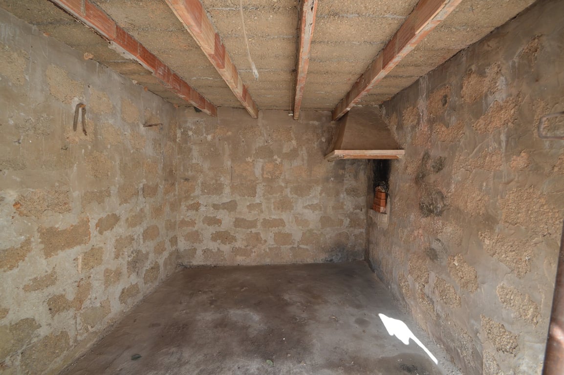 Open space featuring exposed stone walls, wooden ceiling beams, and a rustic corner fireplace, offering potential for conversion into a studio or storage area.