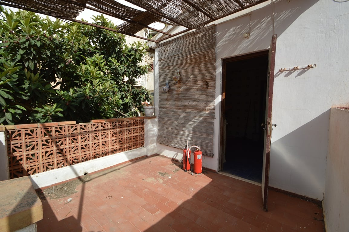 Outdoor terrace featuring terracotta tiling, a reed-covered pergola for shade, and a decorative ceramic breeze block wall adjacent to lush greenery.