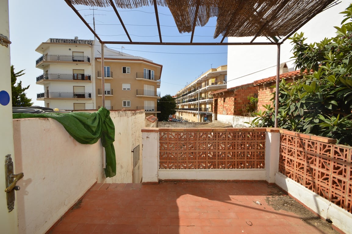 Outdoor terrace featuring terracotta tiling and decorative clay brick latticework, covered by a metal pergola with reed shading overlooking the urban landscape.