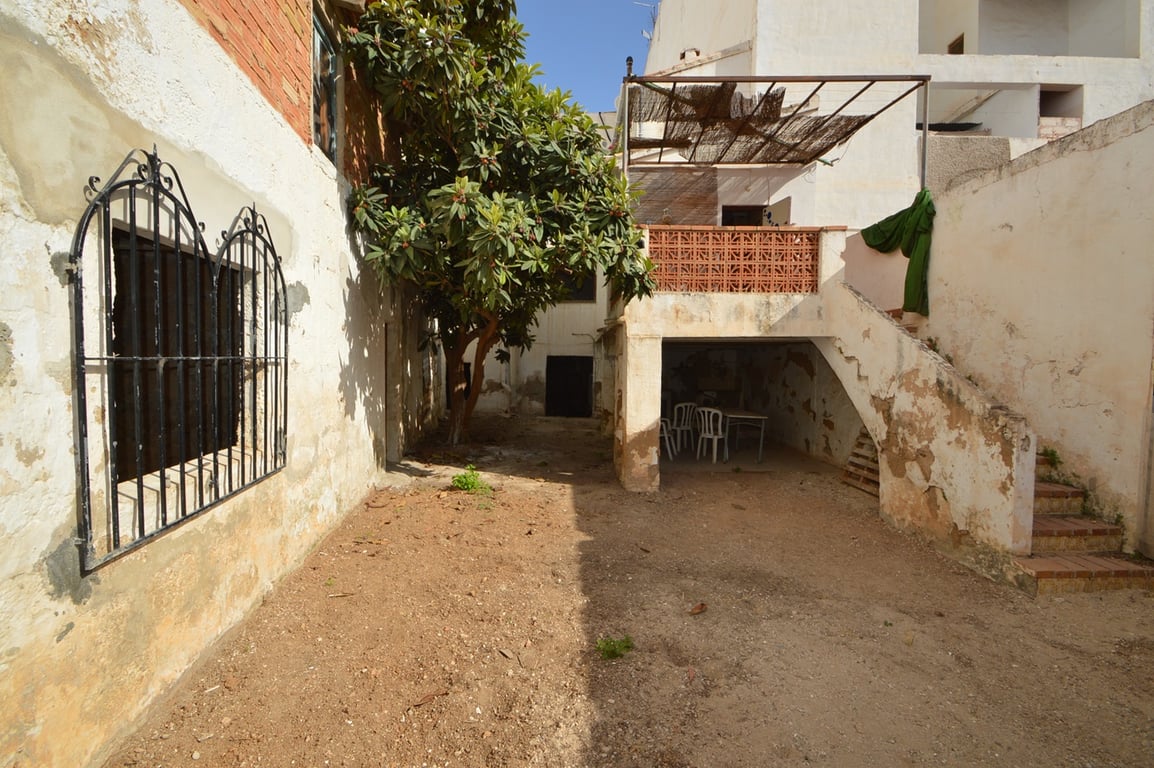 Private earth patio featuring a mature tree, wrought iron window grilles, and stone stairs leading to an upper terrace with a metal pergola structure.