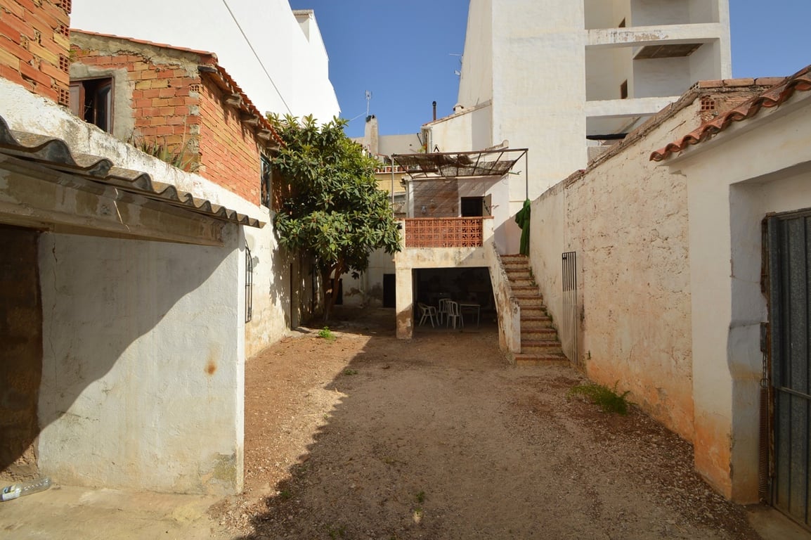 Private interior courtyard featuring earth flooring, high perimeter walls, and an external staircase leading to a raised terrace and shaded porch area.