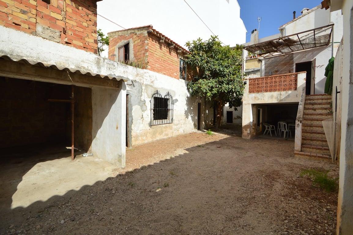 Private interior courtyard featuring unpaved ground, rustic brick outbuildings, and an elevated terrace reached via external stone stairs.