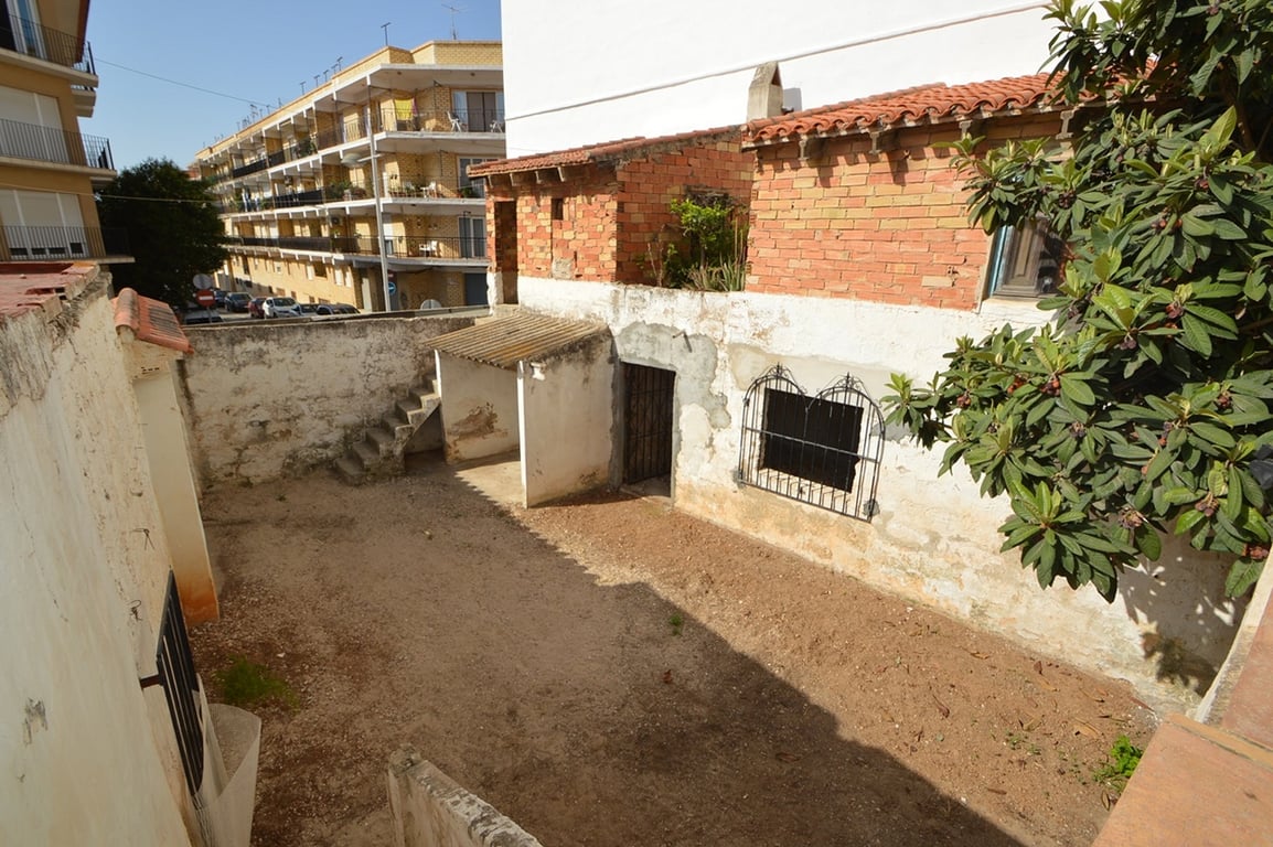 Private walled patio featuring a dirt ground, exposed brick outbuildings with tile roofs, and stone stairs, offering significant renovation potential.