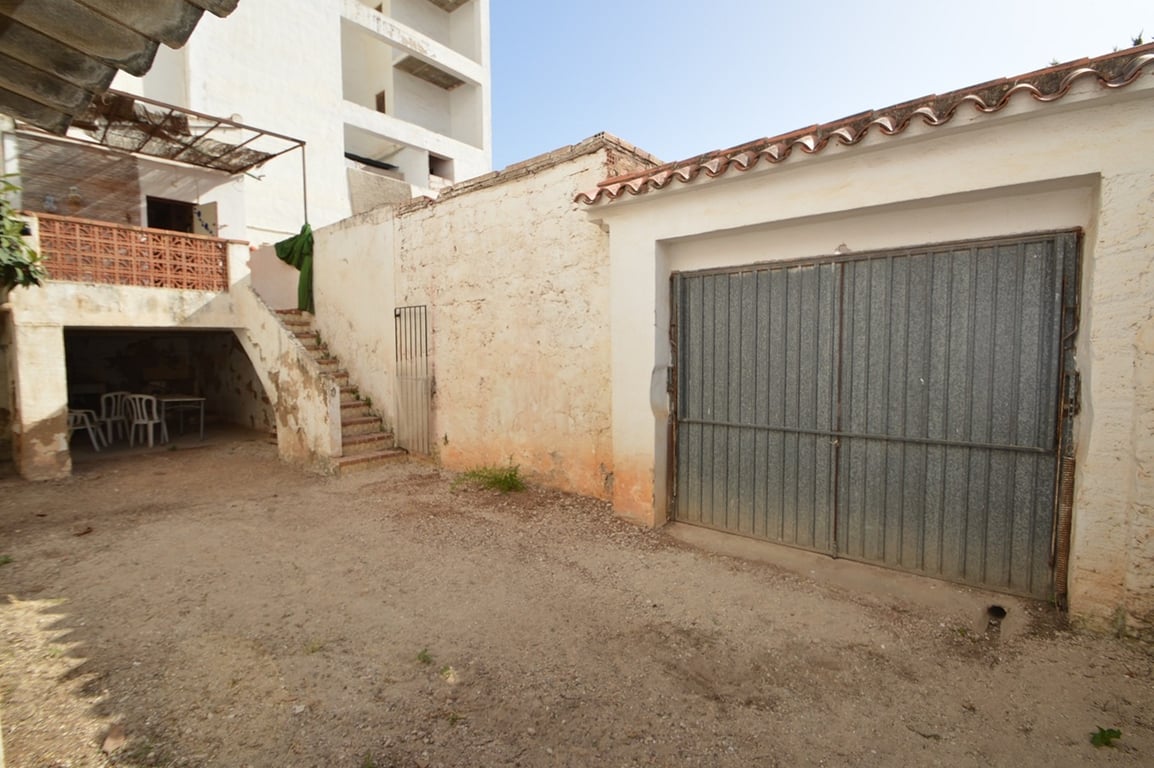Rear patio featuring a metal garage door for private parking, an exterior staircase leading to the upper terrace, and a shaded porch area for storage.