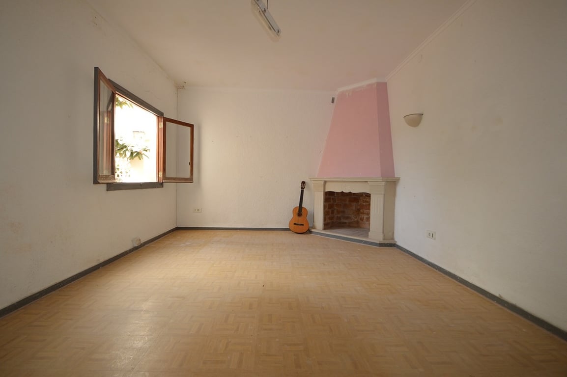 Spacious room featuring a corner fireplace with a pink accent, parquet flooring, and a wooden window opening to the garden area.