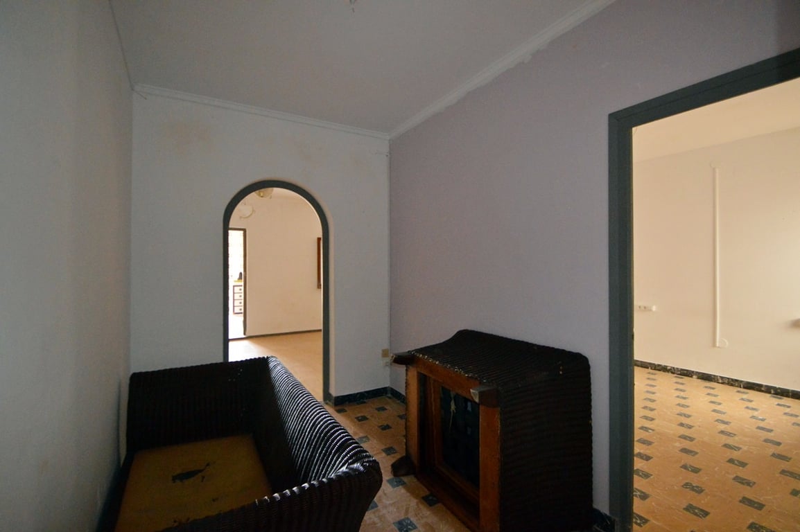 Transitional room featuring original patterned floor tiles, a traditional arched doorway, and access to adjacent bright living spaces.