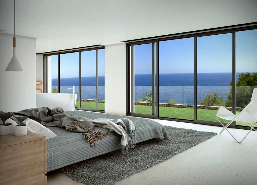 Minimalist bedroom featuring floor-to-ceiling sliding glass doors, grey textiles, and panoramic Mediterranean Sea views overlooking a manicured lawn.