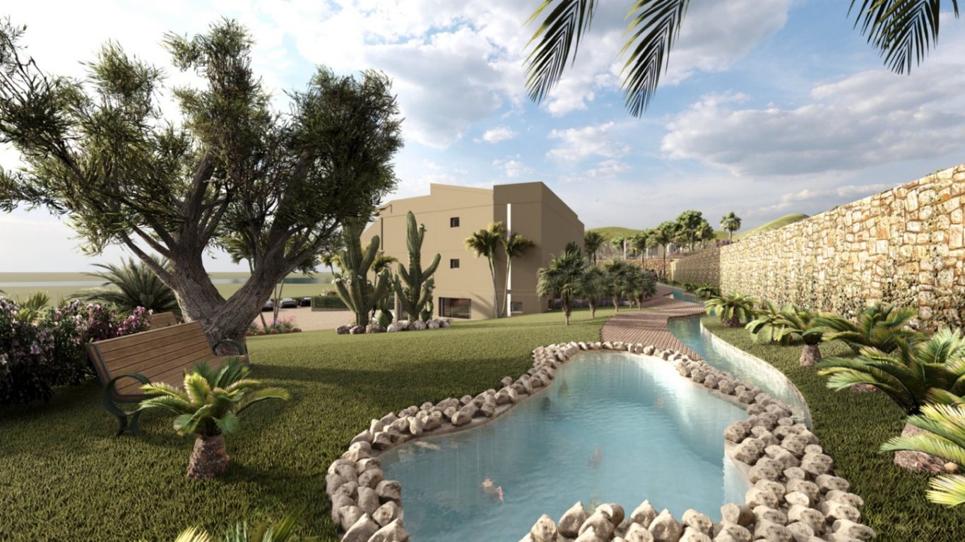 Landscaped gardens featuring a stone-bordered pond, winding paths, and Mediterranean flora including olive trees and cacti adjacent to the hotel structure.