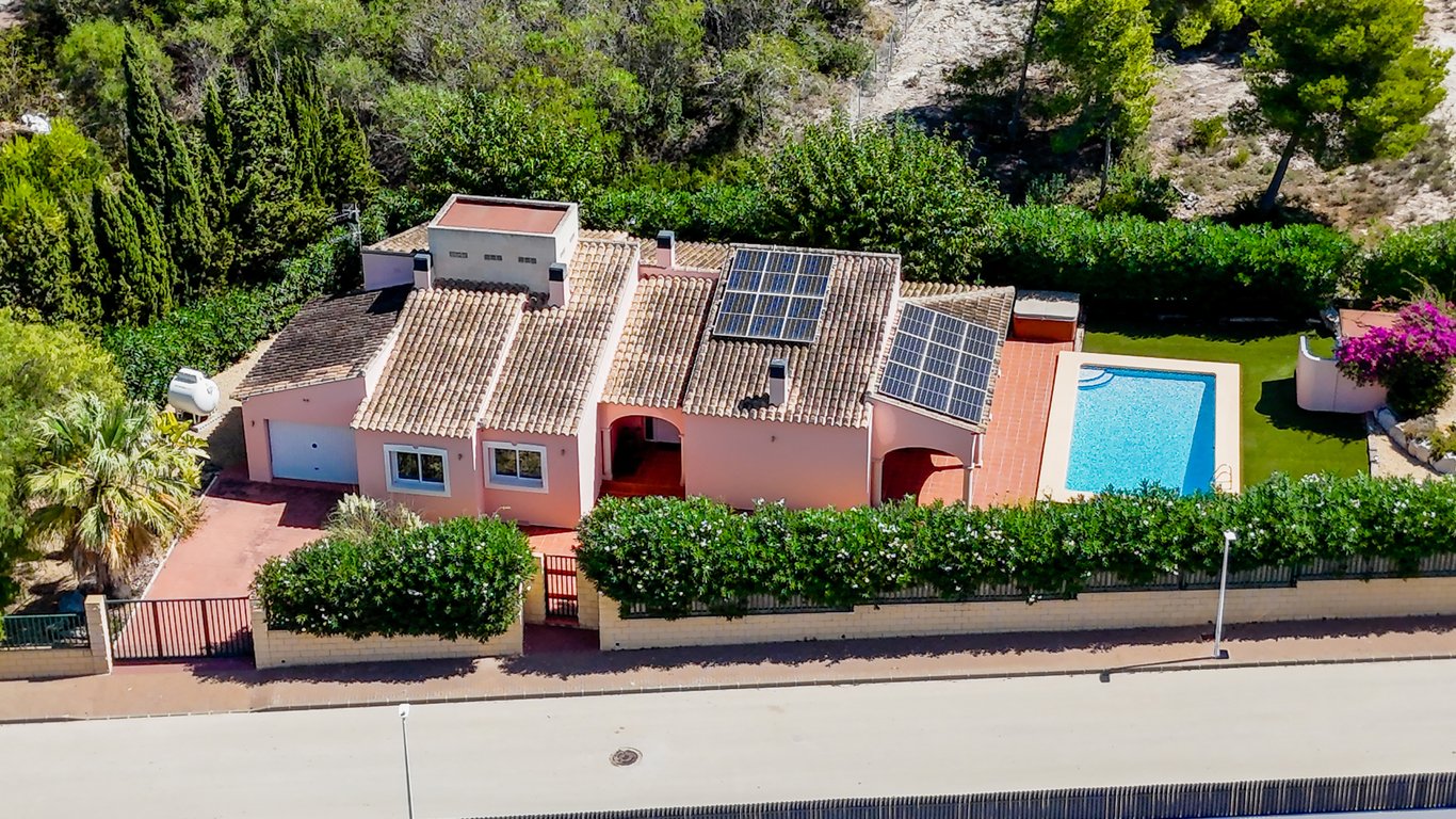 Aerial perspective of the single-level villa, showcasing the private pool, solar panels on the tiled roof, and the secure perimeter with a garage and gated entrance.