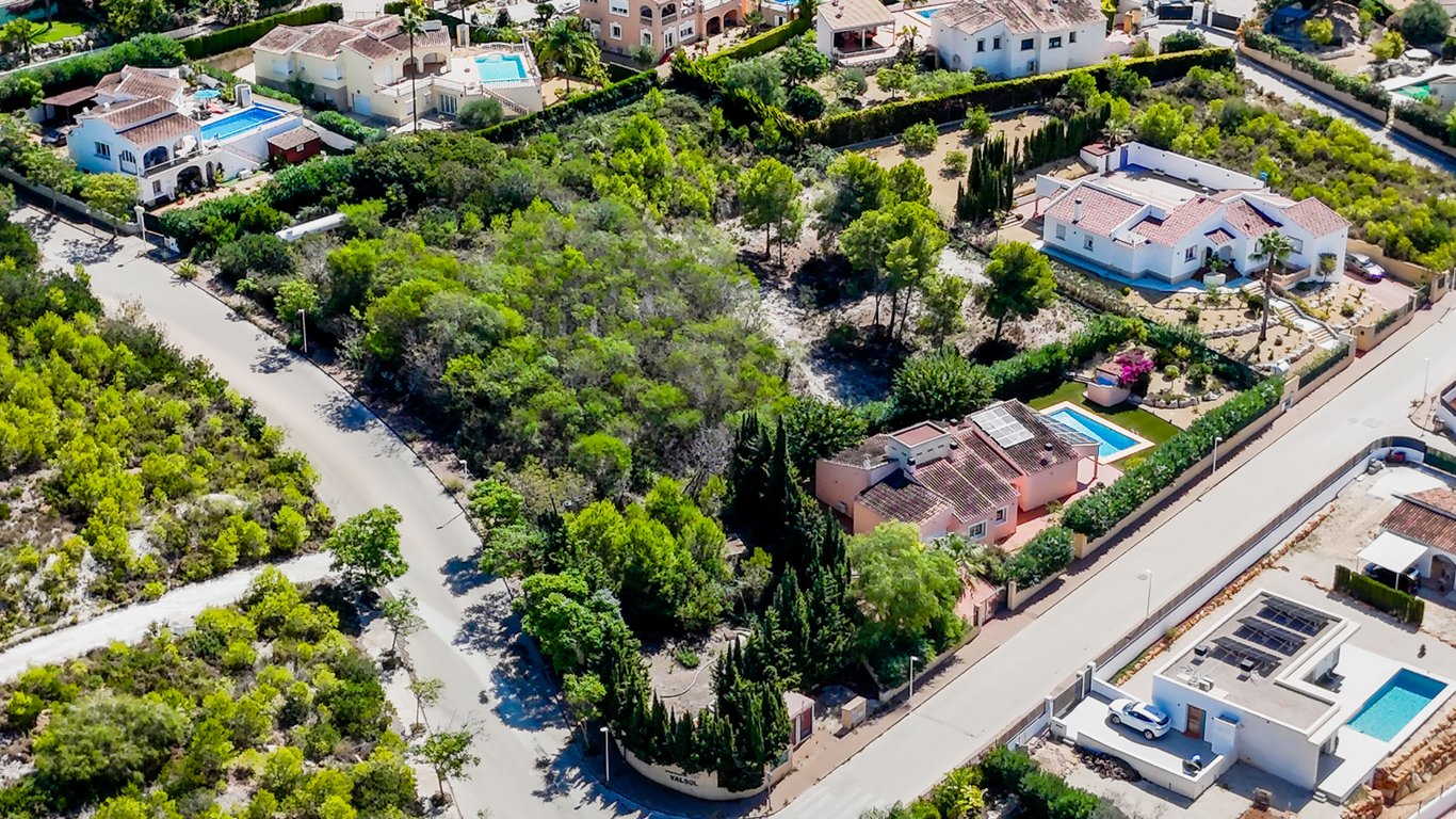Aerial perspective showcasing the single-story layout, private pool, and rooftop solar panels on a fully enclosed flat plot surrounded by greenery.
