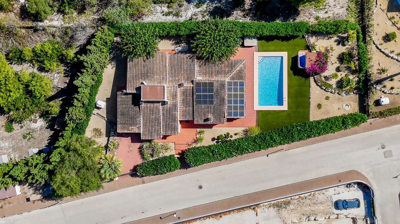 Aerial view of the property featuring the tiled roof with solar panels, a rectangular swimming pool, artificial lawn, and a private jacuzzi area surrounded by hedges.