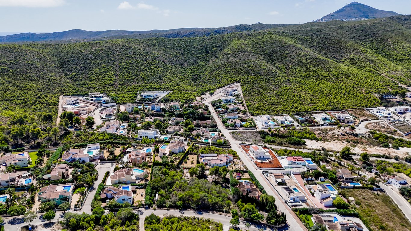Aerial view of the residential area in Jávea, highlighting the villa's peaceful location nestled against lush green mountains and nature.
