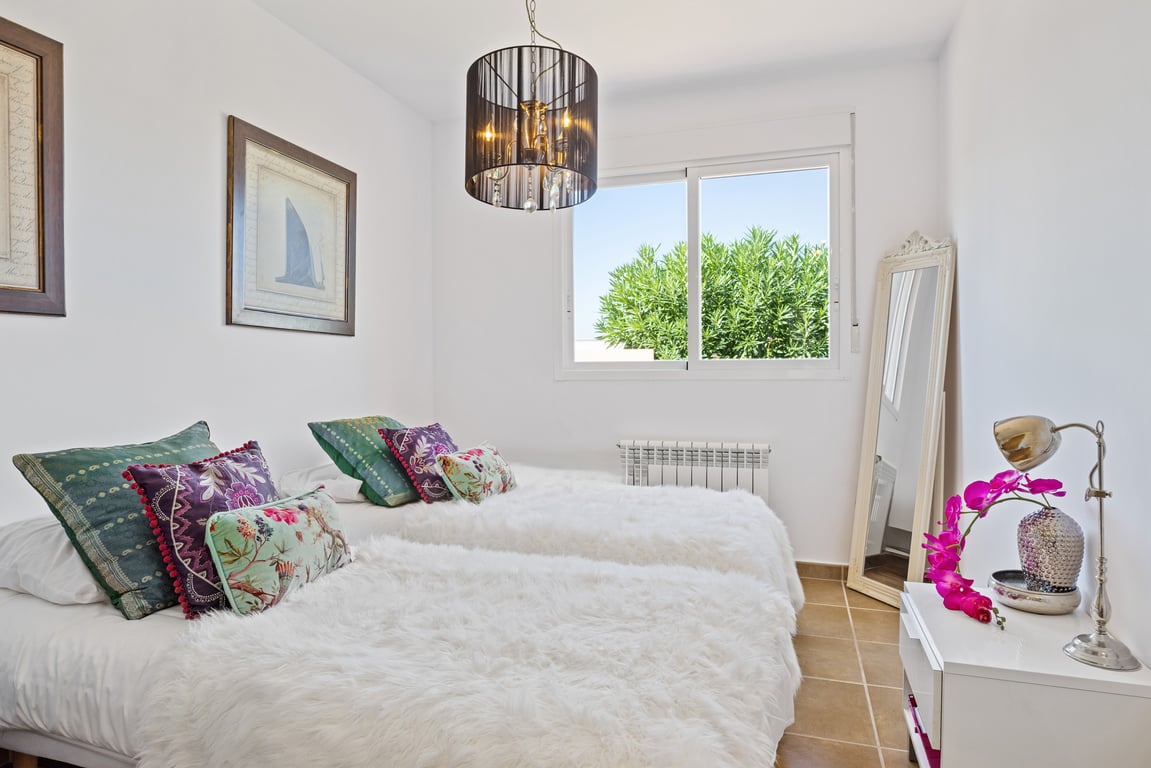 Bright bedroom featuring twin beds, tiled flooring, and a large sliding window with garden views. Equipped with a wall radiator and elegant pendant lighting.