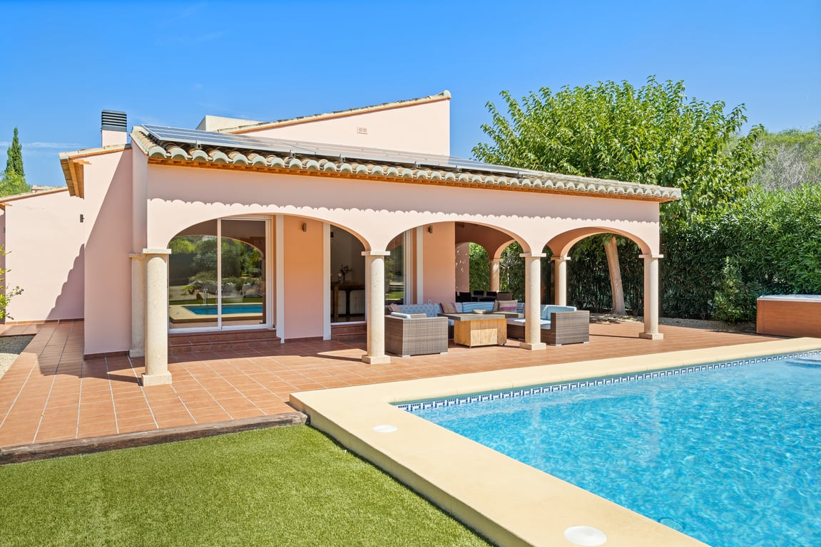 Exterior view featuring a mosaic pool, a spacious naya with stone columns, and solar panels on the roof, complemented by a low-maintenance artificial lawn.