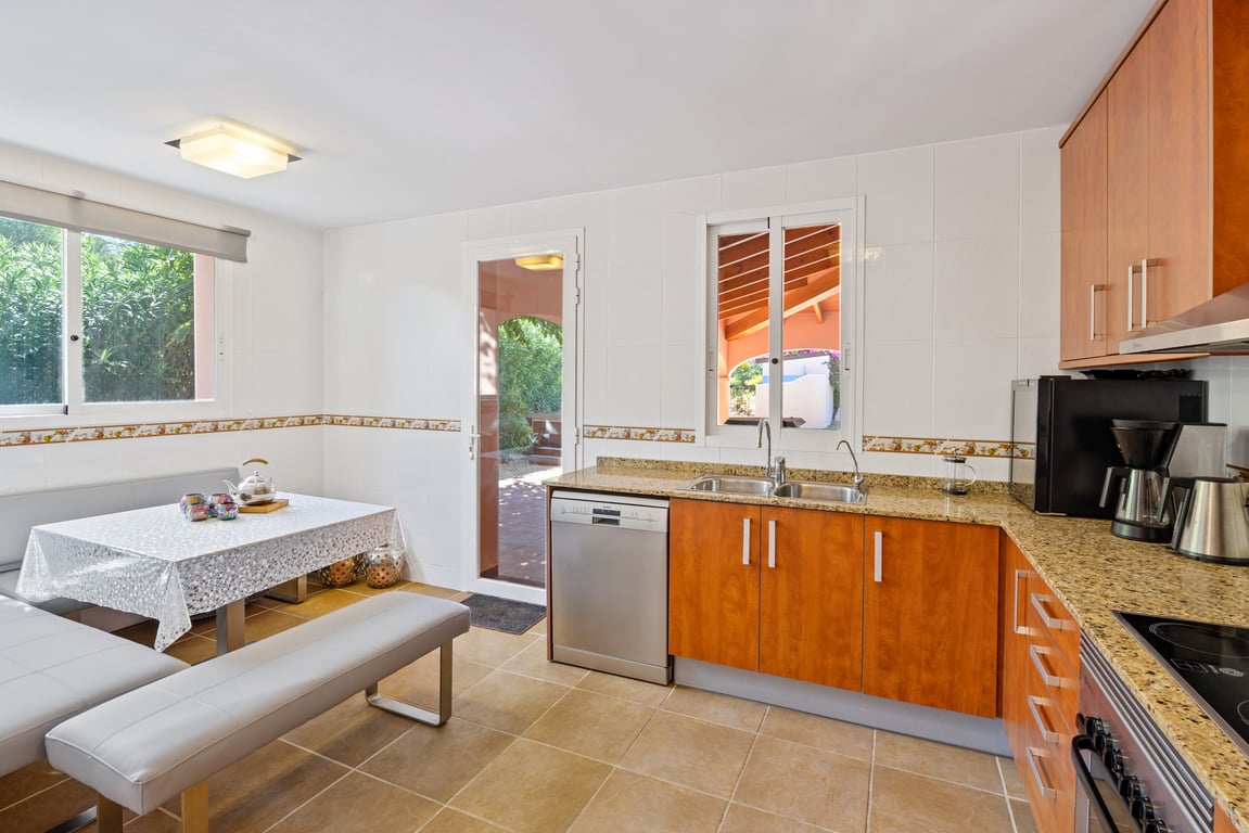 Functional L-shaped kitchen featuring granite countertops, wood cabinetry, and a bright breakfast nook. A glass door provides direct access to the outdoor terrace.