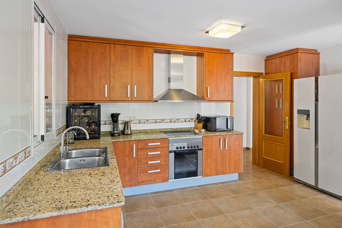 Functional L-shaped kitchen featuring wooden cabinetry, granite countertops, an American-style refrigerator, and integrated appliances including a compact wine cooler.