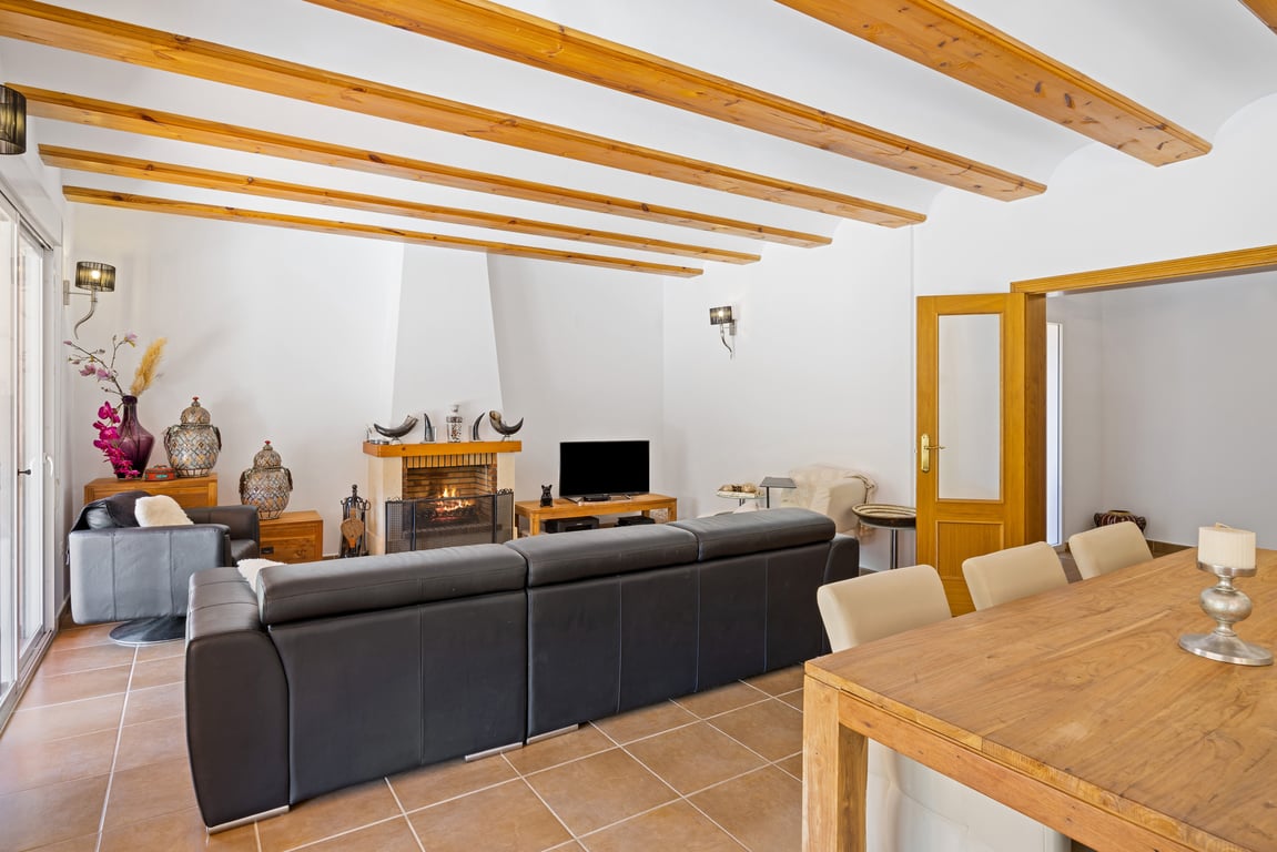 Spacious living-dining room featuring exposed wooden beams, ceramic tile flooring, and a central fireplace with direct access to the outdoor terrace.