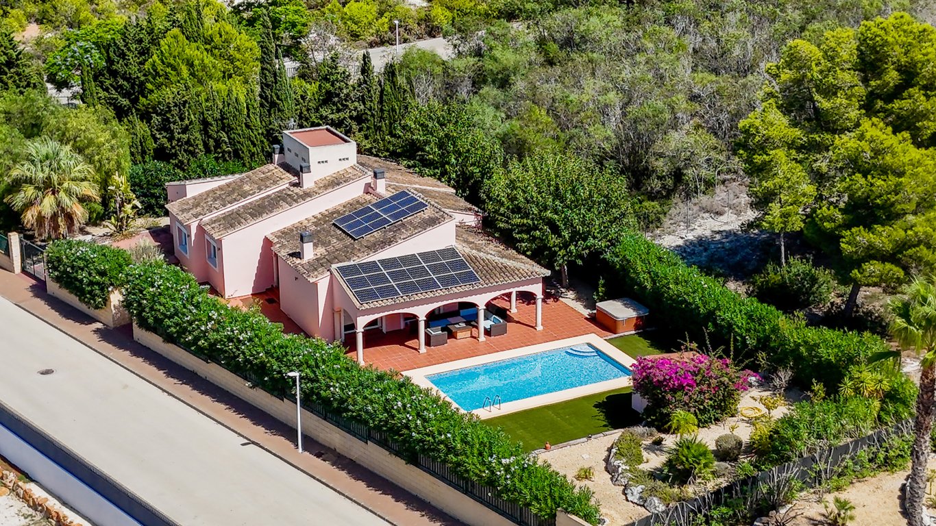 Aerial view of the villa featuring roof-mounted solar panels, an arched naya overlooking the pool, and a landscaped garden with a jacuzzi.