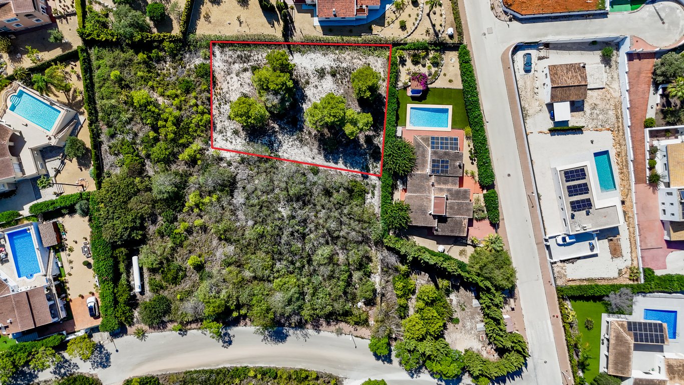 Aerial view of the villa featuring solar panels and a pool, highlighting the adjacent urban building plot outlined in red.