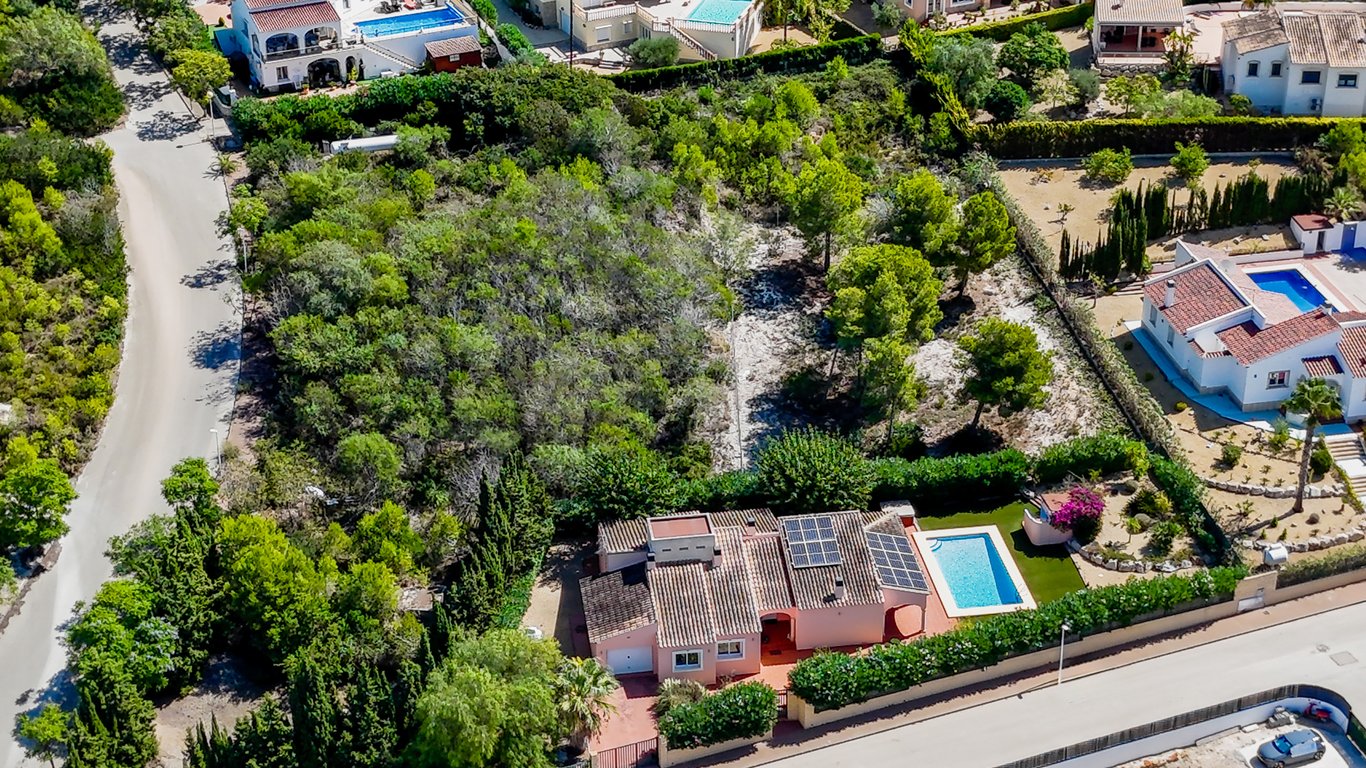 Aerial view showcasing the villa with rooftop solar panels, private pool, and the large adjacent buildable plot with mature Mediterranean trees.