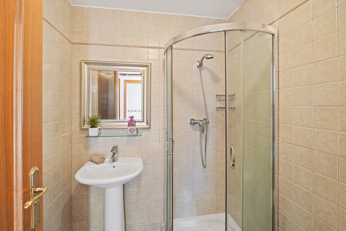 Bathroom featuring a curved glass corner shower, white pedestal sink, and neutral beige wall tiles with a decorative border.