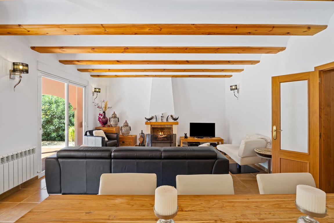 Bright living area featuring exposed wooden ceiling beams, a central fireplace, and direct access to the terrace through sliding glass doors.