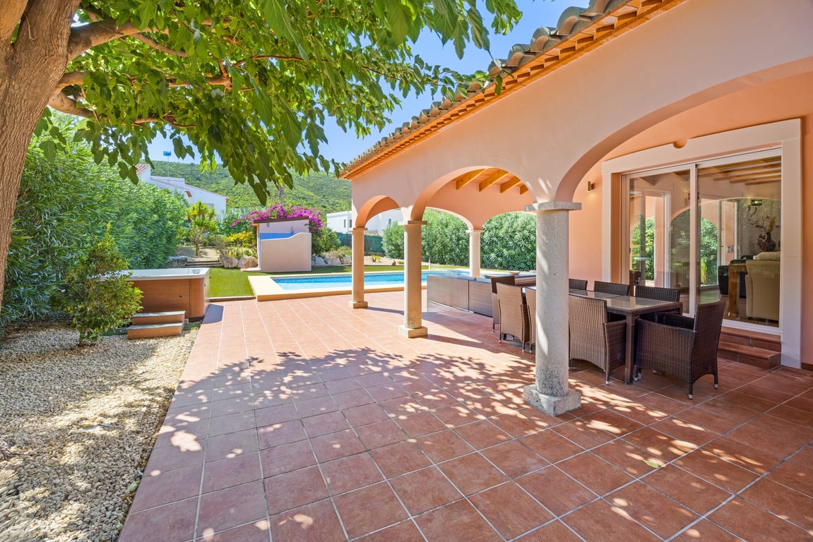 Covered arched naya with stone pillars and wooden beams, featuring an outdoor dining area overlooking the swimming pool, jacuzzi, and Mediterranean garden.