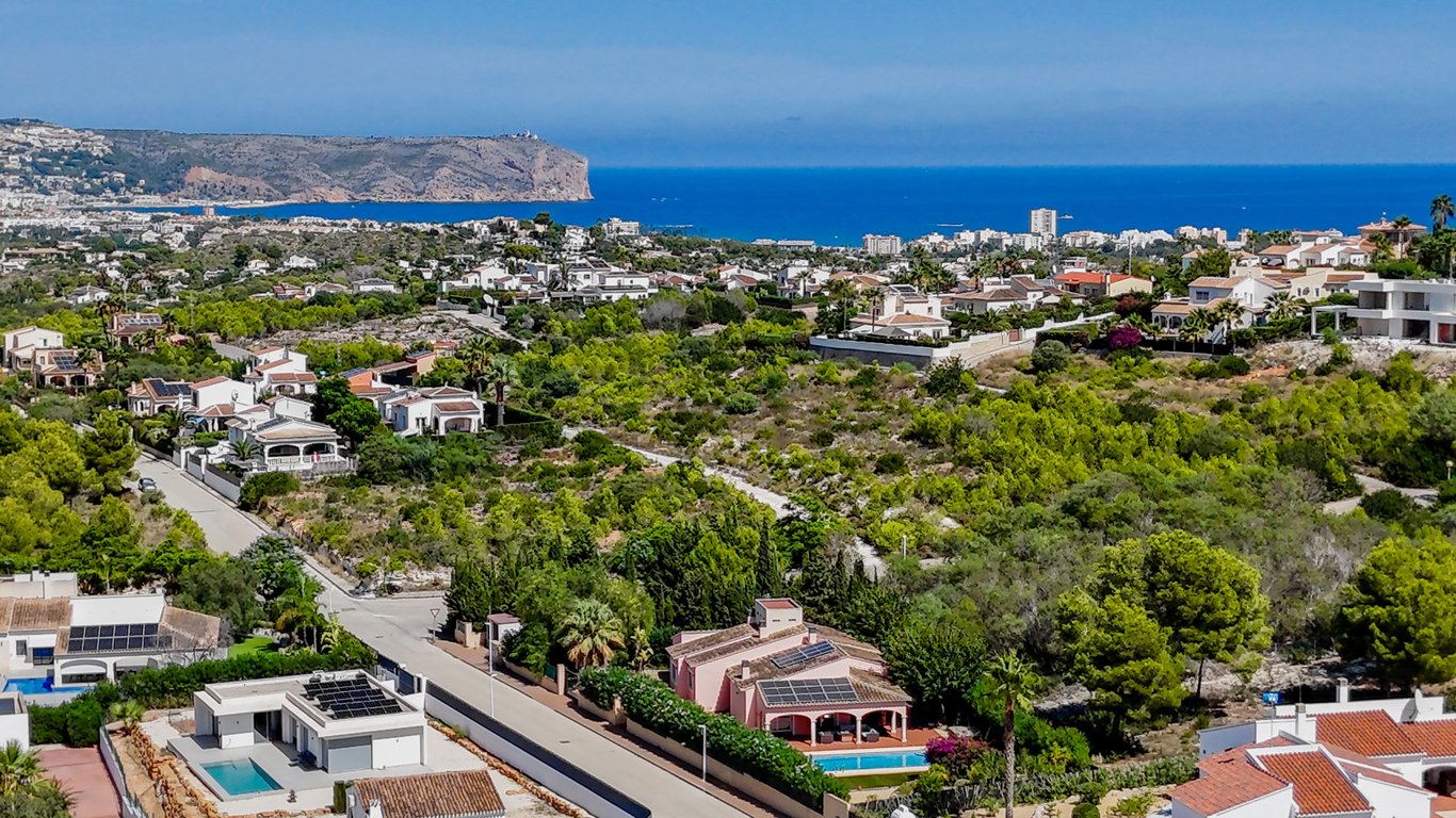 Elevated drone view showing the villa's solar-paneled roof and private pool, set against a backdrop of Mediterranean vegetation and coastal sea views.