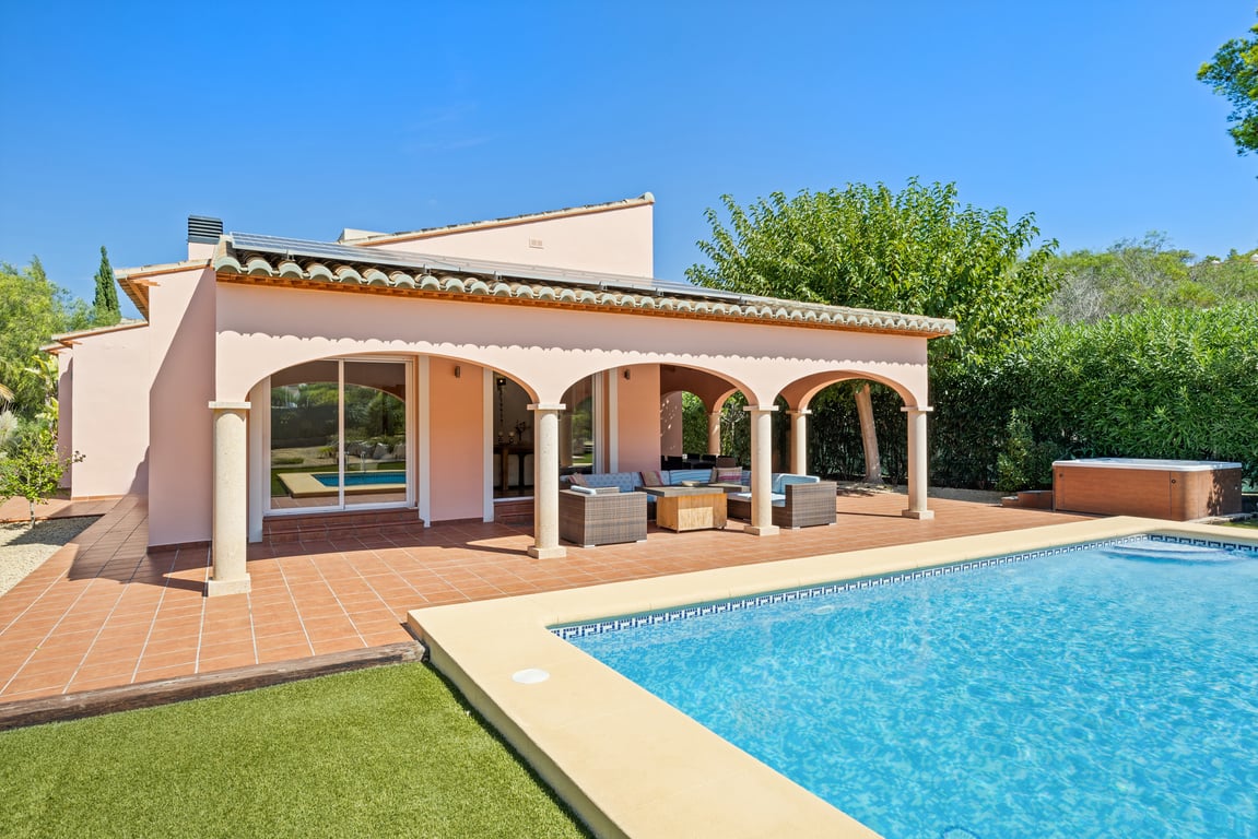 Exterior view of the villa featuring an arched naya with stone pillars, terracotta terrace, mosaic-tiled pool, rooftop solar panels, and outdoor jacuzzi.