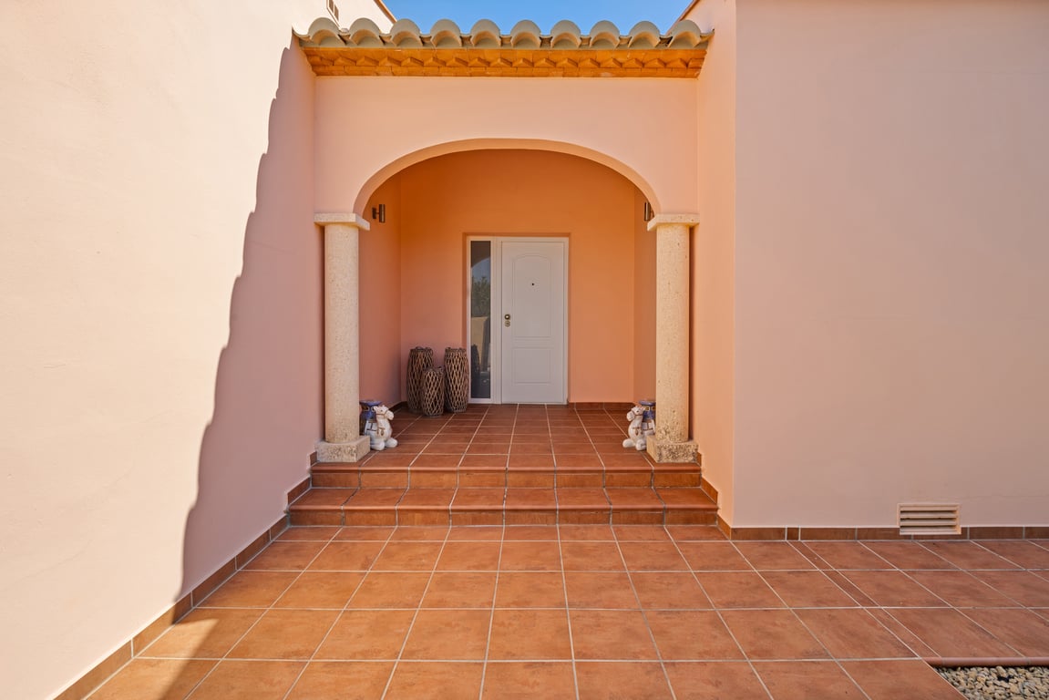 Main entrance featuring an arched porch supported by natural stone columns and terracotta tiling. White front door with a vertical glass side panel.