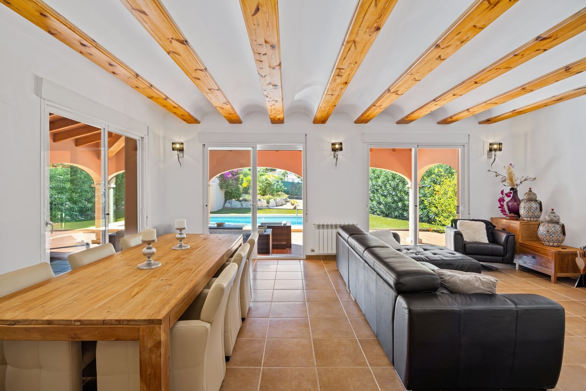 Open-plan living and dining area featuring traditional wooden ceiling beams, terracotta flooring, and large sliding doors opening onto the terrace and pool.