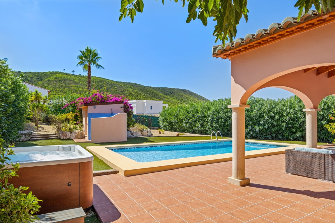 Outdoor terrace featuring a mosaic pool, independent jacuzzi, and arched naya, surrounded by an artificial lawn and scenic mountain views.