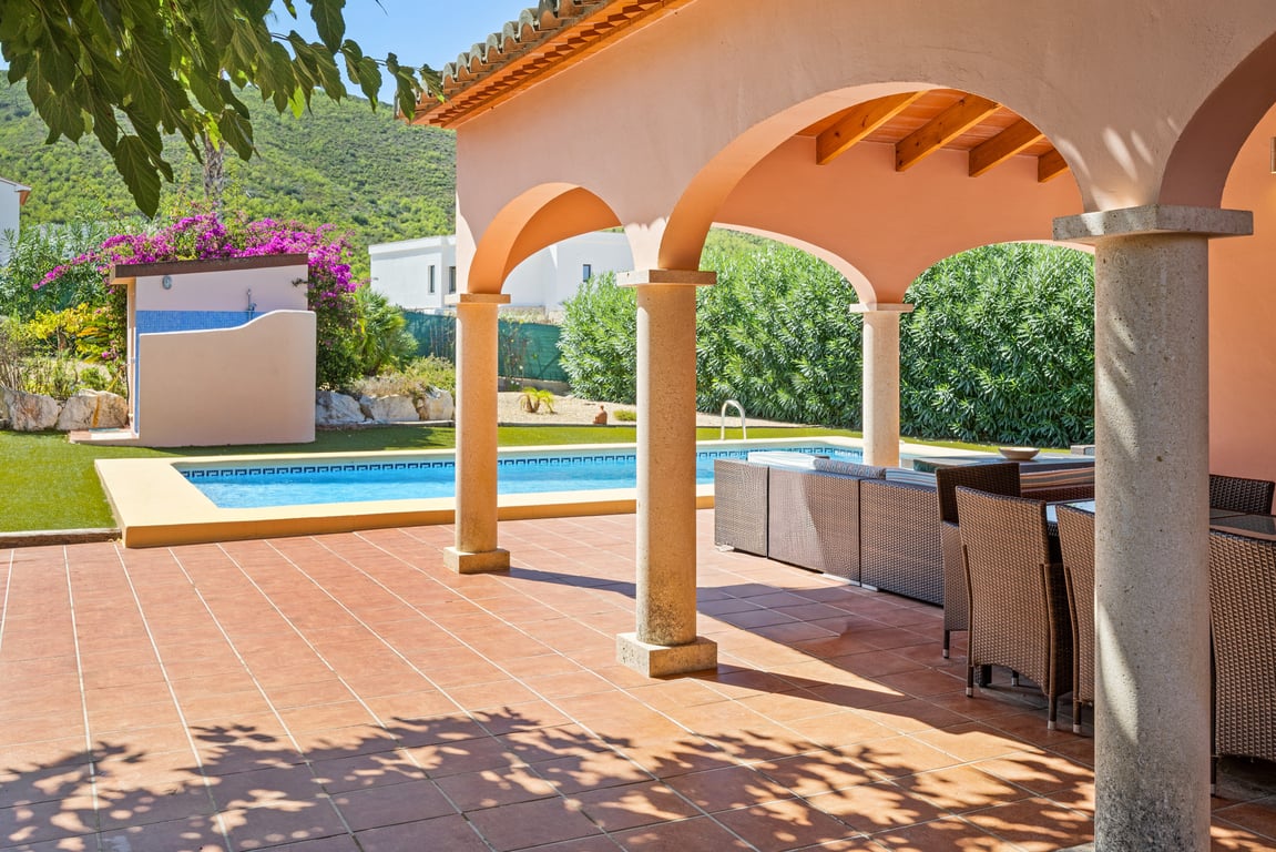 Spacious arched naya featuring stone columns and terracotta tiling, offering views of the mosaic pool, garden, and surrounding mountains.