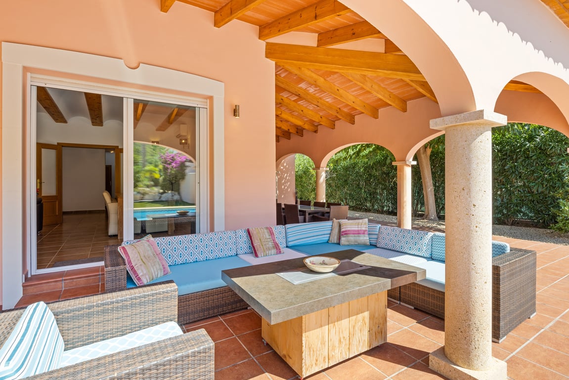 Spacious covered naya featuring exposed wooden beams, stone arches, and a lounge area with wicker furniture on traditional terracotta tiling.