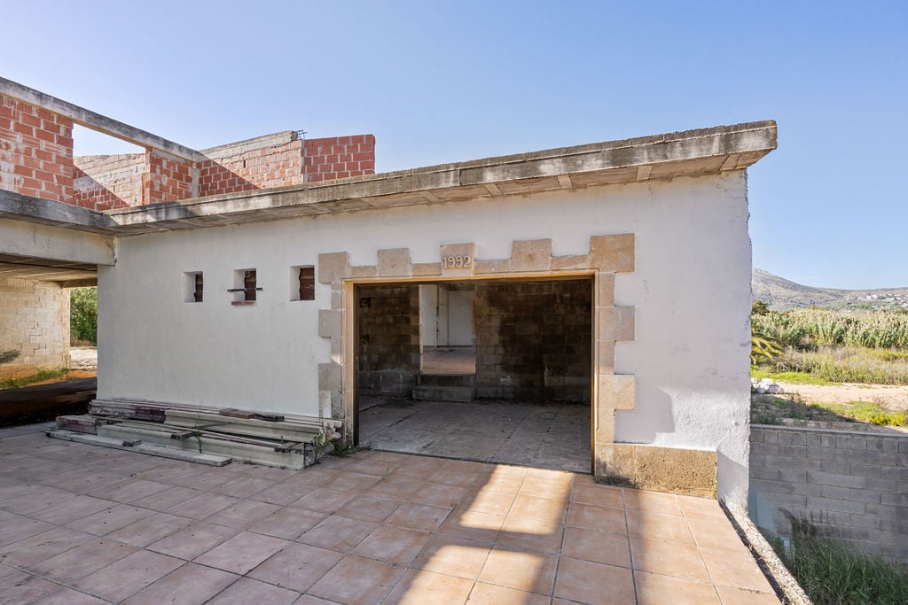 Construction site featuring a tiled terrace, traditional stone framing around the entrance, and a 1992 date inscription on the white facade.