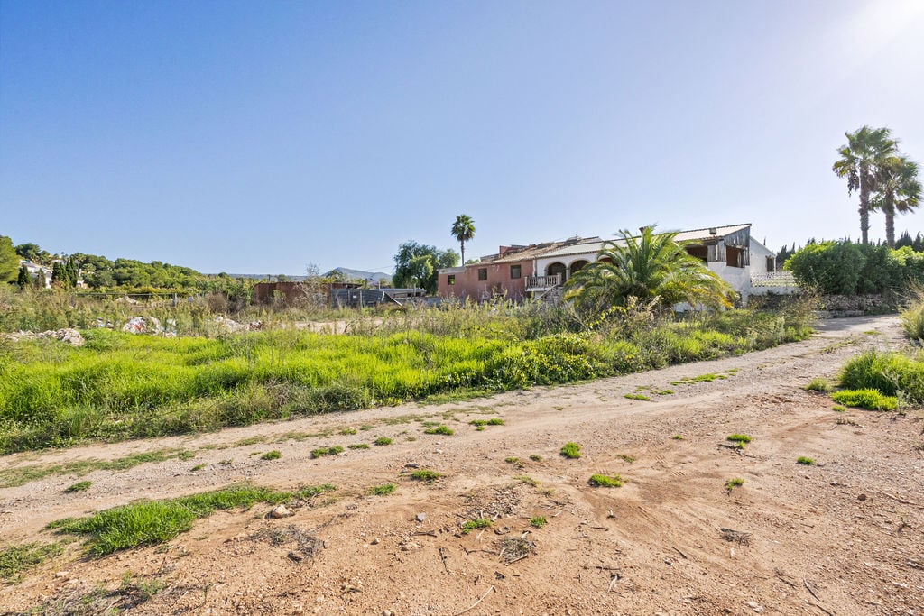 Exterior view of the expansive rustic plot featuring a traditional Mediterranean building with arched porches and native palms under clear skies.
