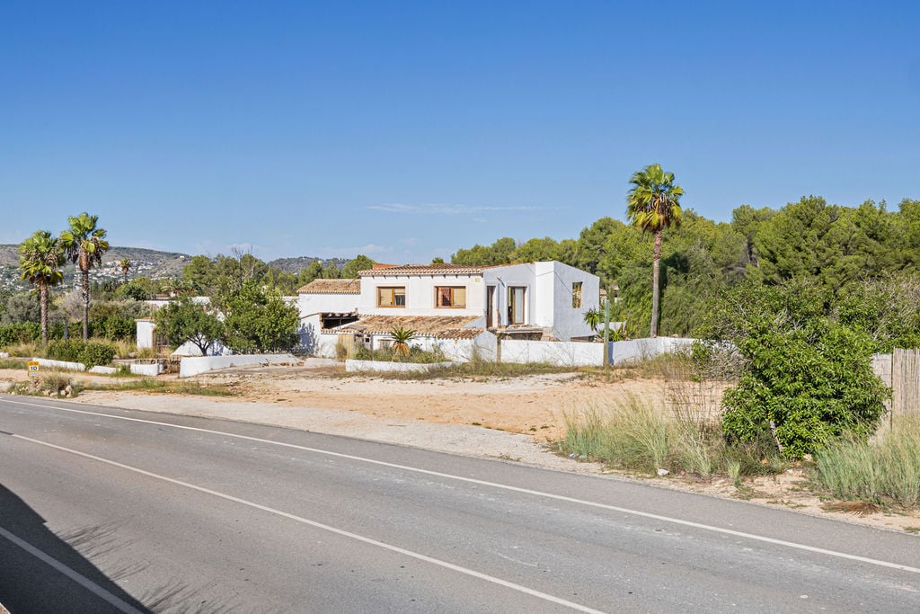 Exterior view of the property from the road, featuring traditional white-walled architecture with clay tile roofs and wooden frames, set against a pine forest.