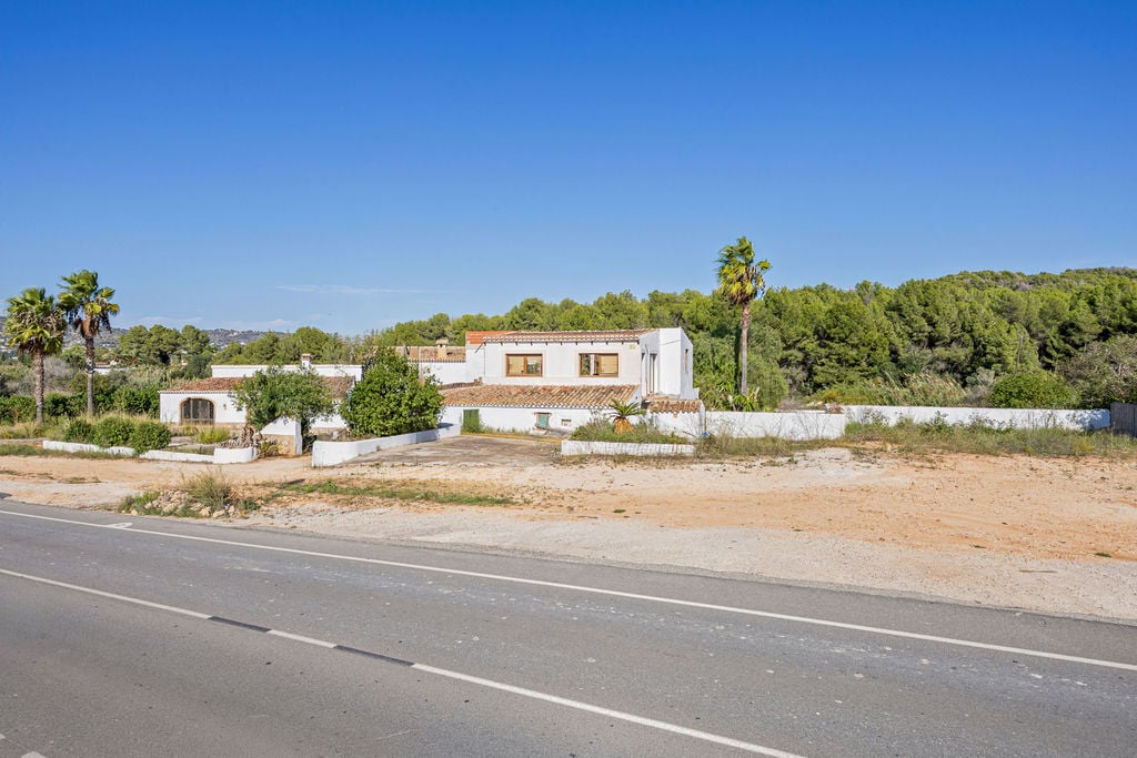 Exterior view of the traditional finca featuring white facades and terracotta roofs, set against a backdrop of pine forests with direct roadside access.