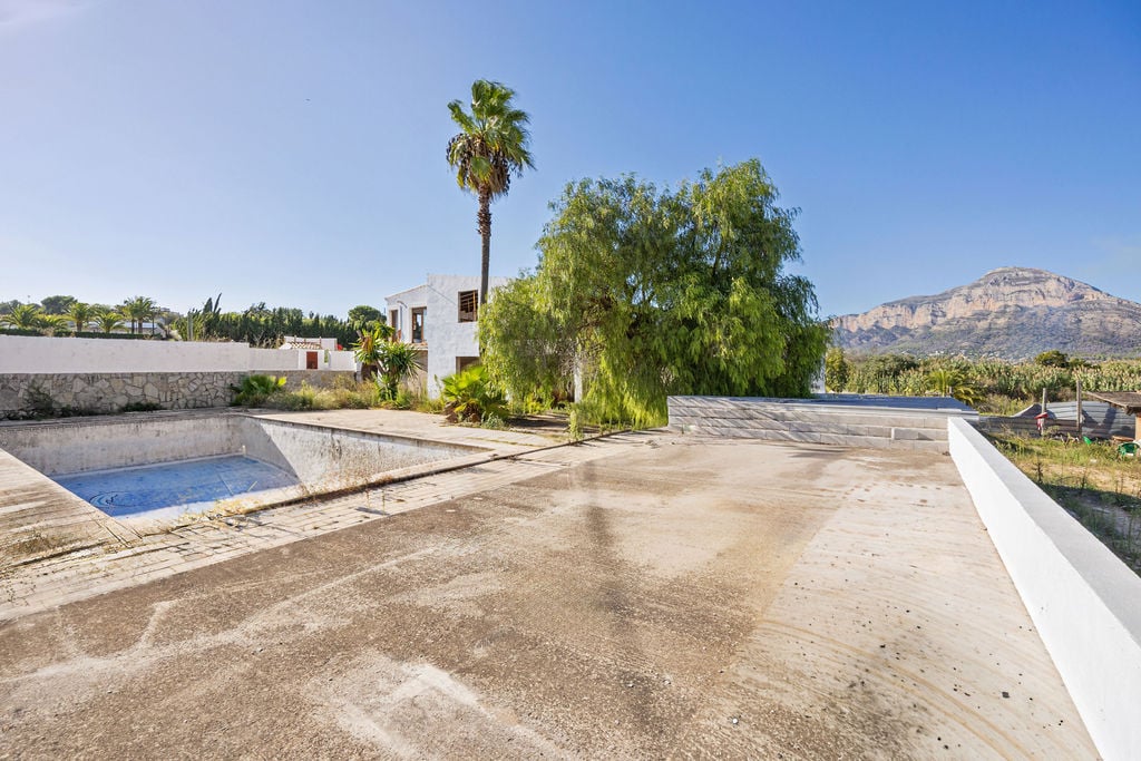 Outdoor concrete terrace with panoramic views of the Montgó mountain, featuring a swimming pool for renovation and a Mediterranean-style building.