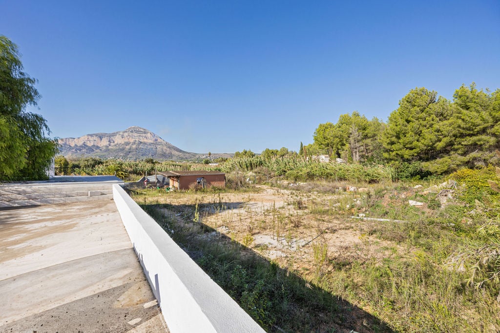 Panoramic view of the Montgó mountain from an elevated concrete terrace, overlooking a flat development plot with native Mediterranean vegetation.