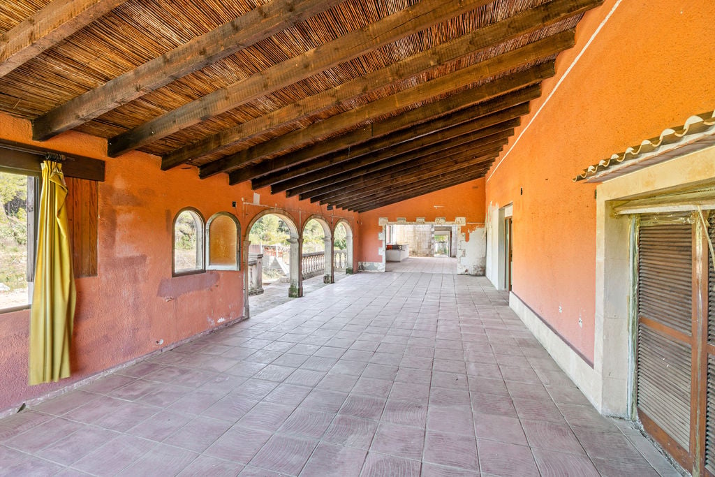 Spacious covered terrace featuring traditional wooden beams with reed ceiling, terracotta walls, and classic stone arches overlooking the grounds.