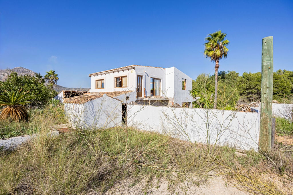 Traditional Mediterranean exterior featuring white-washed walls, terracotta tile roofs, and natural vegetation set against a clear blue sky.